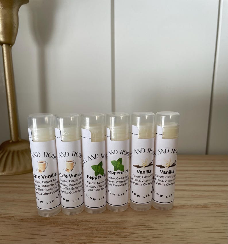 May include: Six clear tubes of lip balm with white labels. The labels have the words "AND ROSE" and the names of the flavors: "Cafe Vanilla", "Peppermint", and "Vanilla".