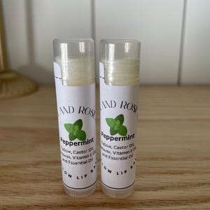 May include: Two white tubes of peppermint lip balm with green leaf designs and the text "Peppermint" and "Tallow, Castor Oil, Beeswax, Vitamin E Oil and Essential Oil" on the labels.
