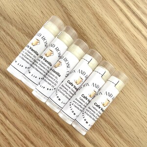 May include: Six white lip balm tubes with labels that say "Cafe Vanilla" and "Vanilla" with a small illustration of a cup of coffee. The labels also list ingredients including beeswax, tallow, castor oil, vitamin E oil, coffee essential oil, and vanilla oleoresin oil.