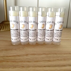 May include: Six white tubes of lip balm with a white label that says "Cafe Vanilla" and lists the ingredients. The label also has a small illustration of a cup of coffee.