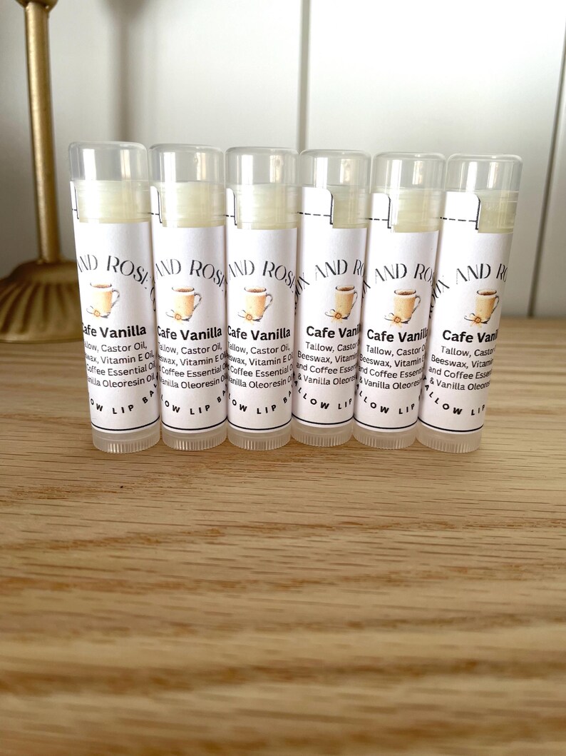 May include: Six white tubes of lip balm with a white label that says "Cafe Vanilla" and lists the ingredients. The label also has a small illustration of a cup of coffee.