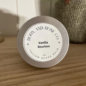May include: A silver tin with a white label that reads "Roux and Rose Co. Vanilla Bourbon 2 oz Beard Balm Tallow"