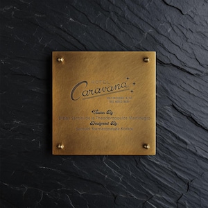 May include: A square brass plaque with four corner studs featuring the engraved text Hotel Caravana, Keep on Rockin in the Free World, Baby, Vision By: Bobby Santini de la Theodoropoulos Martinegro, and Designed By: Samuel Stamatopatata Korkos.