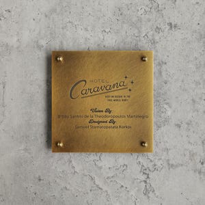 May include: A square brushed brass plaque with four corner screws. The text reads: HOTEL Caravana, KEEP ON ROCKIN' IN THE FREE WORLD, BABY!, Vision By: Bobby Santini de la Theodoropoulos Martinegro, Designed By: Samuel Stamatopatata Korkos.