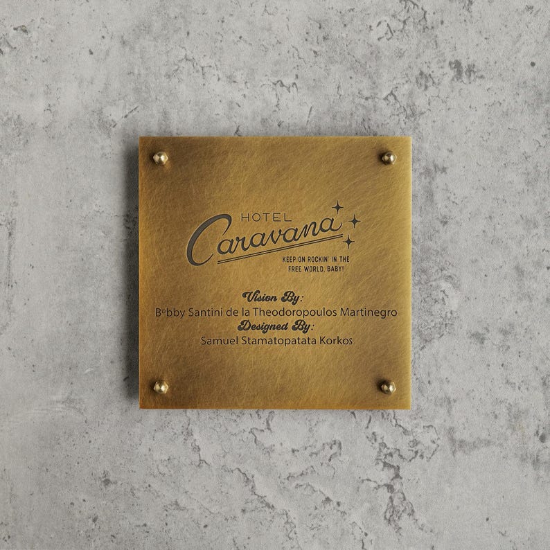 May include: A square brushed brass plaque with four corner screws. The text reads: HOTEL Caravana, KEEP ON ROCKIN' IN THE FREE WORLD, BABY!, Vision By: Bobby Santini de la Theodoropoulos Martinegro, Designed By: Samuel Stamatopatata Korkos.