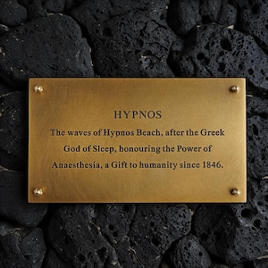 May include: A rectangular brass plaque with four small corner screws, featuring the engraved text: HYPNOS. The waves of Hypnos Beach, after the Greek God of Sleep, honouring the Power of Anaesthesia, a Gift to humanity since 1846.