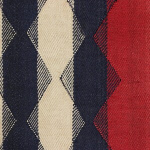 May include: Close-up of a woven fabric with a geometric pattern. The design features alternating vertical stripes of cream, navy blue, and red. The texture of the fabric is visible, suggesting a textured material.