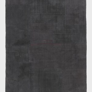 May include: A dark gray patchwork rug with a rectangular shape. The rug is composed of various rectangular and square pieces of fabric sewn together. The color is a solid, muted gray, with subtle variations in tone across the surface.