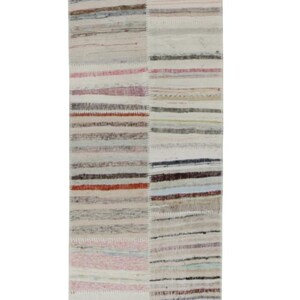 Pode incluir: Um tapete retangular com um design de patchwork. O tapete apresenta listras horizontais em várias cores, incluindo bege, rosa, vermelho e azul. O tapete tem aproximadamente 152 cm de comprimento e 76 cm de largura.