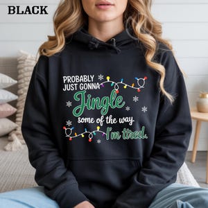 May include: Black hooded sweatshirt with the text "PROBABLY JUST GONNA Jingle some of the way. I'm tired." The text is in white and green with snowflake and Christmas light accents. The word "BLACK" is at the top left.