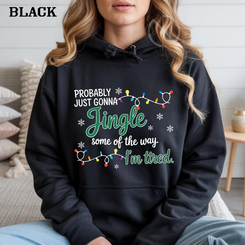May include: Black hooded sweatshirt with the text "PROBABLY JUST GONNA Jingle some of the way. I'm tired." The text is in white and green with snowflake and Christmas light accents. The word "BLACK" is at the top left.