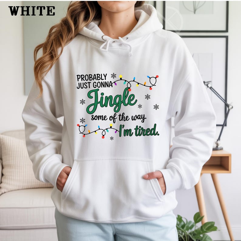 May include: White hooded sweatshirt with the text "PROBABLY JUST GONNA Jingle some of the way. I'm tired." The design includes a string of colorful Christmas lights and snowflakes. The word "WHITE" is in the upper left corner.