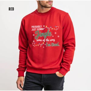 May include: A red sweatshirt with the text "Probably just gonna Jingle some of the way I'm tired." The text is in white and green with a string of Christmas lights and snowflakes. The word "RED" is in the top left corner.
