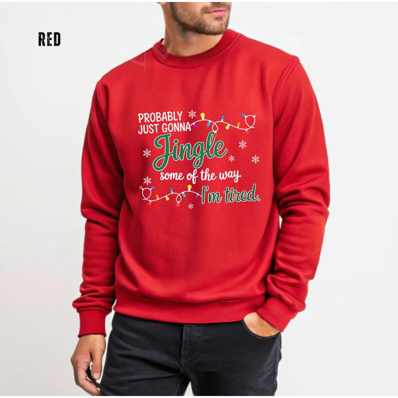 May include: A red sweatshirt with the text "Probably just gonna Jingle some of the way I'm tired." The text is in white and green with a string of Christmas lights and snowflakes. The word "RED" is in the top left corner.