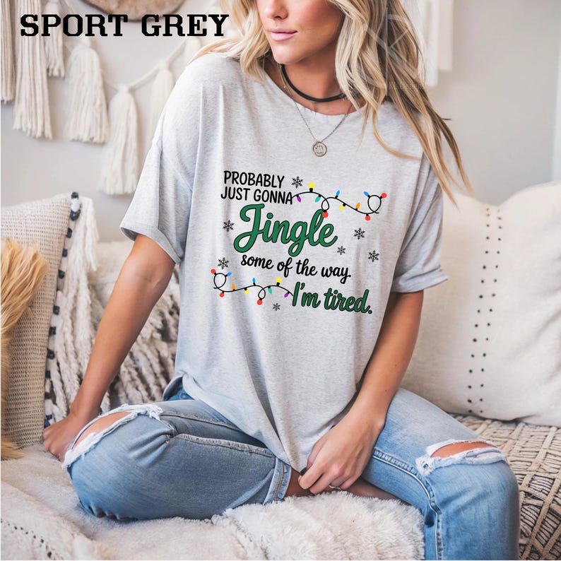 May include: Sport grey t-shirt with the text "Probably Just Gonna Jingle some of the way, I'm tired." The text is in green and black with a string of Christmas lights. The shirt is a short-sleeved, casual style.