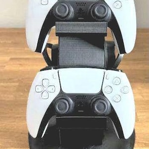 Peut inclure: Deux manettes de jeu sans fil blanches sont montées sur un support de charge noir. Les manettes sont connectées au support et sont en charge.