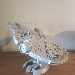 Op de afbeelding: Een wit plastic model van het ruimteschip Millennium Falcon uit Star Wars. Het model staat op een standaard met een Rebel Alliance-symbool.