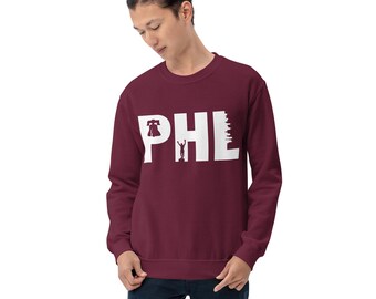 Puede incluir: Una sudadera color burdeos con un gráfico blanco de las letras "PHL" con una Campana de la Libertad y una silueta del horizonte de Filadelfia.