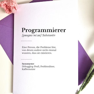 May include: A white greeting card with black text featuring the German word Programmierer, its phonetic pronunciation, and a definition describing a person who solves problems others did not know existed, placed on a purple envelope.