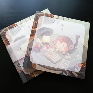 Może przedstawiać: Brązowa i biała małpa z zakręconym ogonem siedzi przy stole z książką, filiżanką herbaty i kawałkiem ciasta. Małpa ma na sobie białą koszulę i czarny krawat. Stół jest ozdobiony lampą, wazą z kwiatami i stosem książek. Tło to jasnoniebieska ściana z białym sufitem.