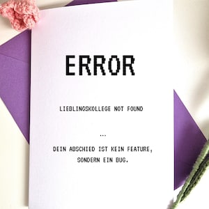 Könnte beinhalten: Eine weiße Karte mit dem Wort "ERROR" in großen, pixeligen schwarzen Buchstaben. Darunter steht der Text "LIEBLINGSKOLLEGE NOT FOUND" und "DEIN ABSCHIED IST KEIN FEATURE, SONDERN EIN BUG." Die Karte befindet sich in einem lila Umschlag, mit gehäkelten rosa Blumen.