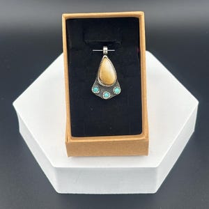 Op de afbeelding: Een traanvormige hanger met een bruine steen gezet in zilver, geaccentueerd met vier turquoise stenen.