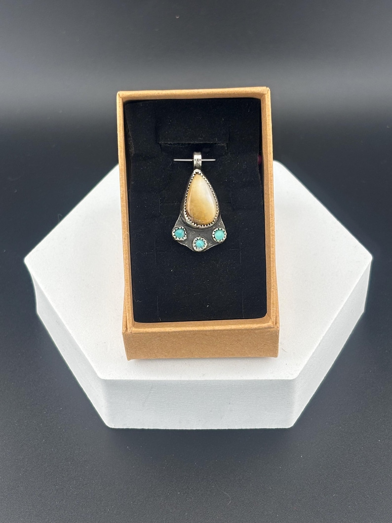 Op de afbeelding: Een traanvormige hanger met een bruine steen gezet in zilver, geaccentueerd met vier turquoise stenen.