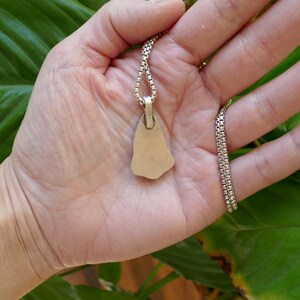 Op de afbeelding: Een zilveren ketting met een gladde, onregelmatig gevormde hanger. De hanger is bevestigd aan een zilveren ketting.