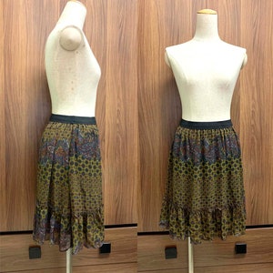 May include: A green and brown patterned skirt with a black waistband and a ruffled hem. The skirt is made of a sheer fabric and has a paisley design.