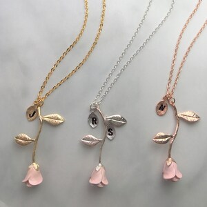 May include: Three gold, silver, and rose gold necklaces with a delicate rose pendant. Each rose has a single initial charm on the stem. The initials are J, R, and N.