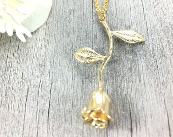 Peut inclure: Un collier en or avec une rose, composé d'une chaîne délicate et d'un pendentif en forme de rose. La rose est ornée de feuilles et d'une tige.