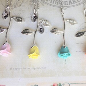 May include: Five silver rose necklaces with different colored rose charms. The roses are pink, yellow, turquoise, peach, and red.
