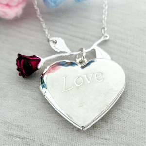 Peut inclure: Un collier avec un pendentif en forme de cœur argenté avec le mot "Love" gravé sur le devant. Une petite rose rouge et argentée est attachée au médaillon. Le collier est sur une chaîne argentée.