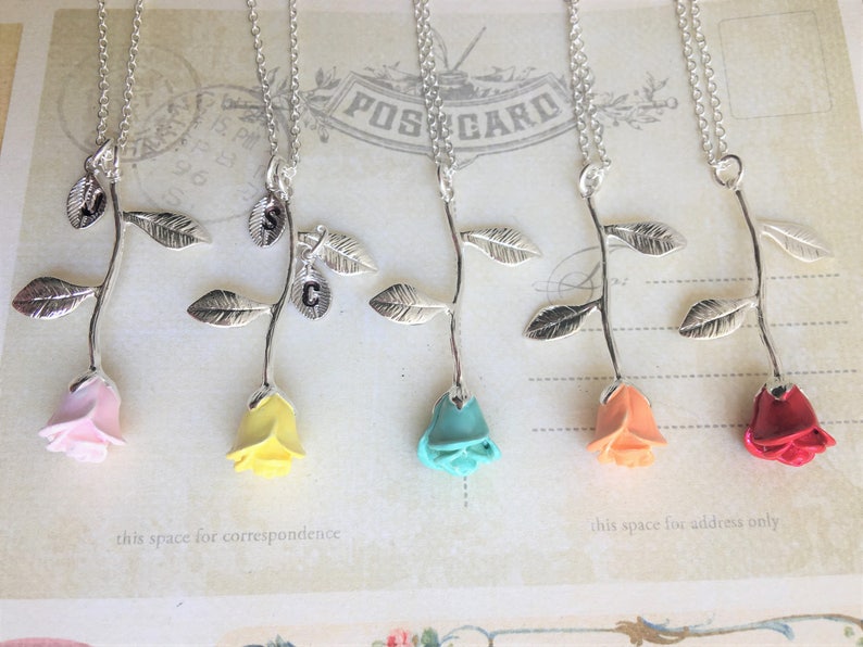 May include: Five silver rose necklaces with different colored rose charms. The roses are pink, yellow, turquoise, peach, and red.