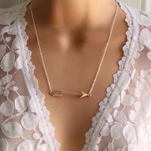 May include: A silver chain necklace with a gold arrow pendant. The arrow is a simple design with a pointed tip and a straight line.