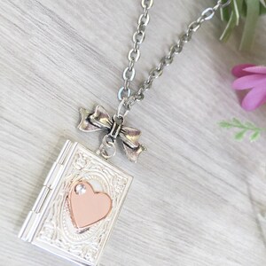 May include: Silver-toned locket necklace with a bow accent. The locket is rectangular with an embossed design and a pink heart in the center. The chain is a linked style. A small crystal is set above the heart.