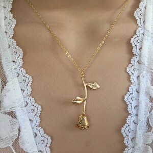 May include: A gold rose pendant necklace on a model wearing a white lace top.