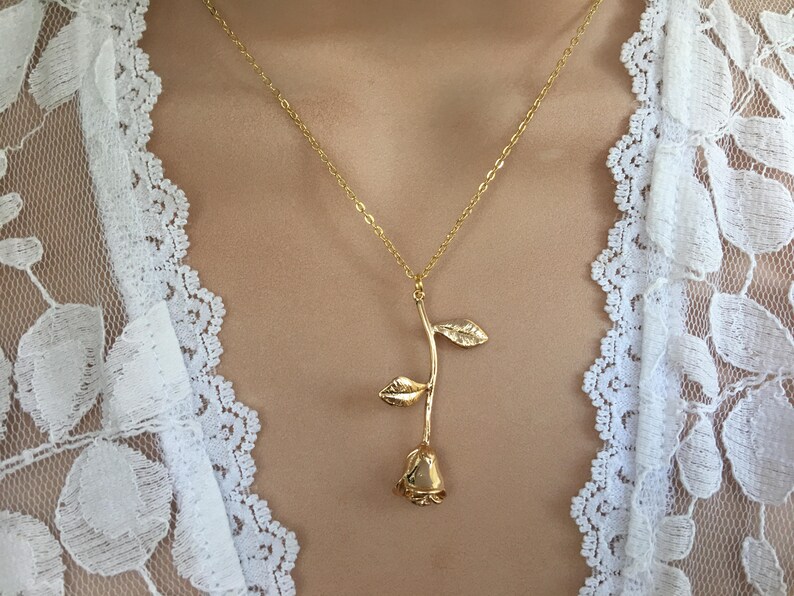 May include: A gold rose pendant necklace on a model wearing a white lace top.