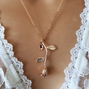 May include: A gold chain necklace with a rose pendant. The rose is made of gold and has a single leaf on each side. The pendant has a small charm with the letter "S" on it.