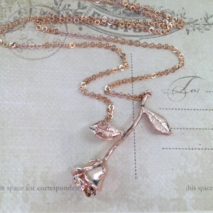 May include: A rose gold necklace with a rose pendant. The rose has a long stem and two leaves. The chain is a delicate, cable chain.