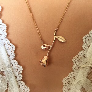 May include: A gold rose necklace with a delicate chain and a simple rose pendant.