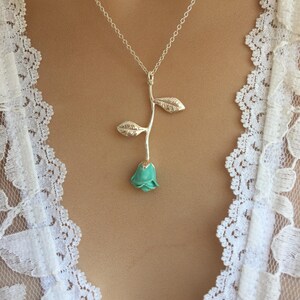 May include: A silver chain necklace with a turquoise blue rose pendant. The rose has a silver stem and leaves.
