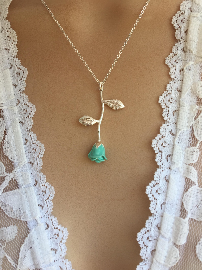 May include: A silver chain necklace with a turquoise blue rose pendant. The rose has a silver stem and leaves.