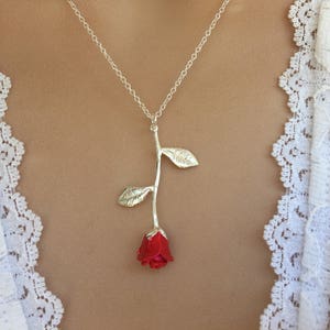May include: A silver necklace with a red rose pendant. The rose is detailed with leaves and a stem.