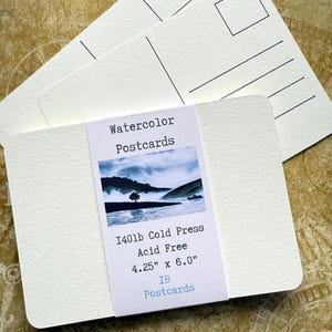 May include: A stack of white watercolor postcards with rounded corners, labeled "Watercolor Postcards." The label also indicates the paper is 140lb cold press, acid-free, and measures 4.25" x 6.0". The label features a landscape image and the text "18 Postcards."