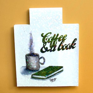 May include: A watercolor illustration featuring a steaming coffee mug, a green book, and the text "Coffee & a book" in green glitter. The artwork is on a white background with glitter accents.