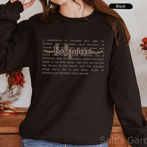 K&ouml;nnte beinhalten: Schwarzes Sweatshirt mit Rundhalsausschnitt und dem Wort "holyween" in Schreibschrift. Das Sweatshirt enth&auml;lt auch ein Gedicht &uuml;ber Holyween. Ein bequemer, l&auml;ssiger Stil.