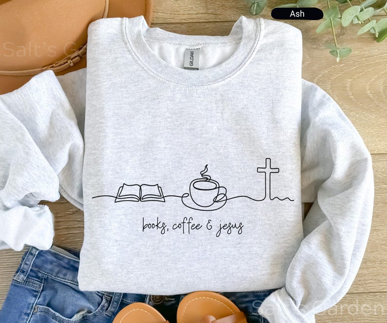 May include: Ash gray sweatshirt with a black line drawing of an open book, coffee cup, and cross. The words "books, coffee & jesus" are written below the drawing. The sweatshirt is made of a soft material.