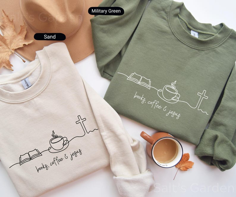 May include: Two crewneck sweatshirts, one sand-colored and one military green, are displayed. Each features a minimalist line drawing of an open book, coffee cup, and cross, with the text "books, coffee & jesus" in a script font. A hat and a mug are also visible.
