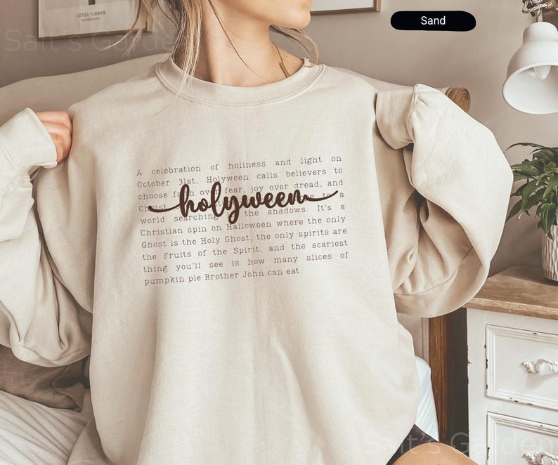 K&ouml;nnte beinhalten: Ein sandfarbenes Sweatshirt mit dem Wort "holyween" in einer Schreibschrift. Das Sweatshirt hat einen Rundhalsausschnitt und lange &Auml;rmel. Der Text auf dem Shirt beschreibt eine christliche Variante von Halloween.
